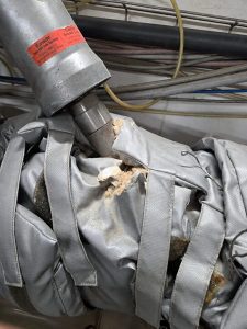 Damaged removable insulation blanket with exposed insulation fibres around process equipment